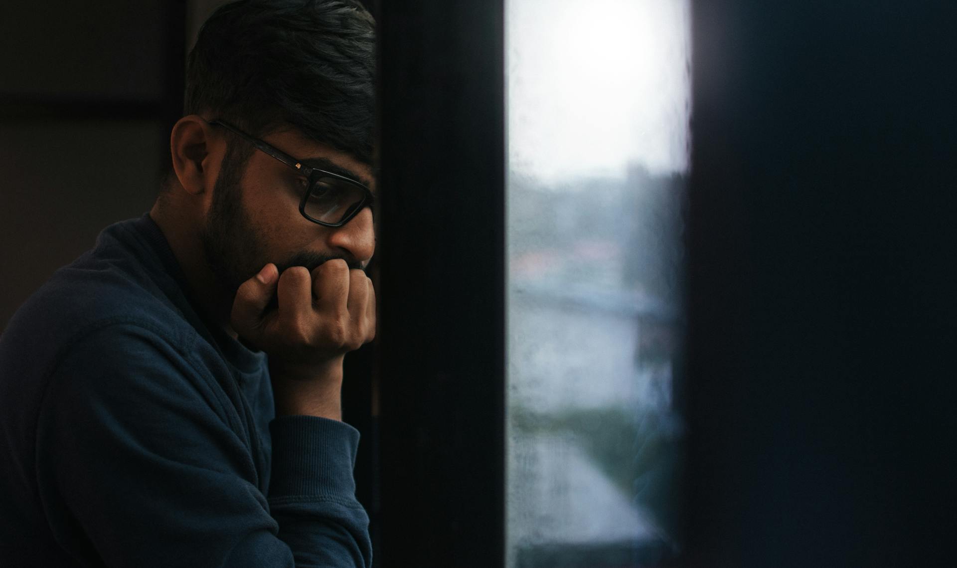 Homem pensativo observa pela janela enquanto reflete sobre saúde mental na rotina corrida