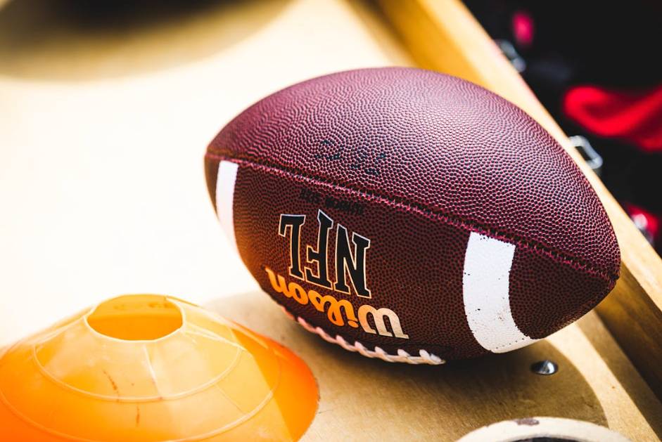 Bola oficial da NFL sobre mesa de madeira ao lado de cone de treino em ambiente esportivo