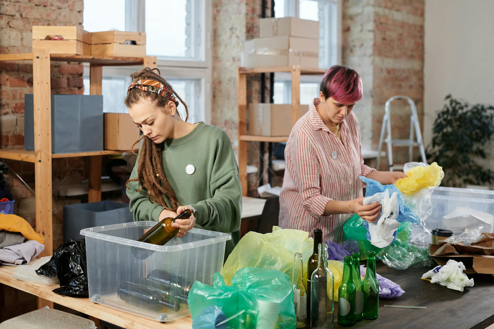 Duas pessoas separando vidros e plásticos recicláveis em ambiente de trabalho sustentável