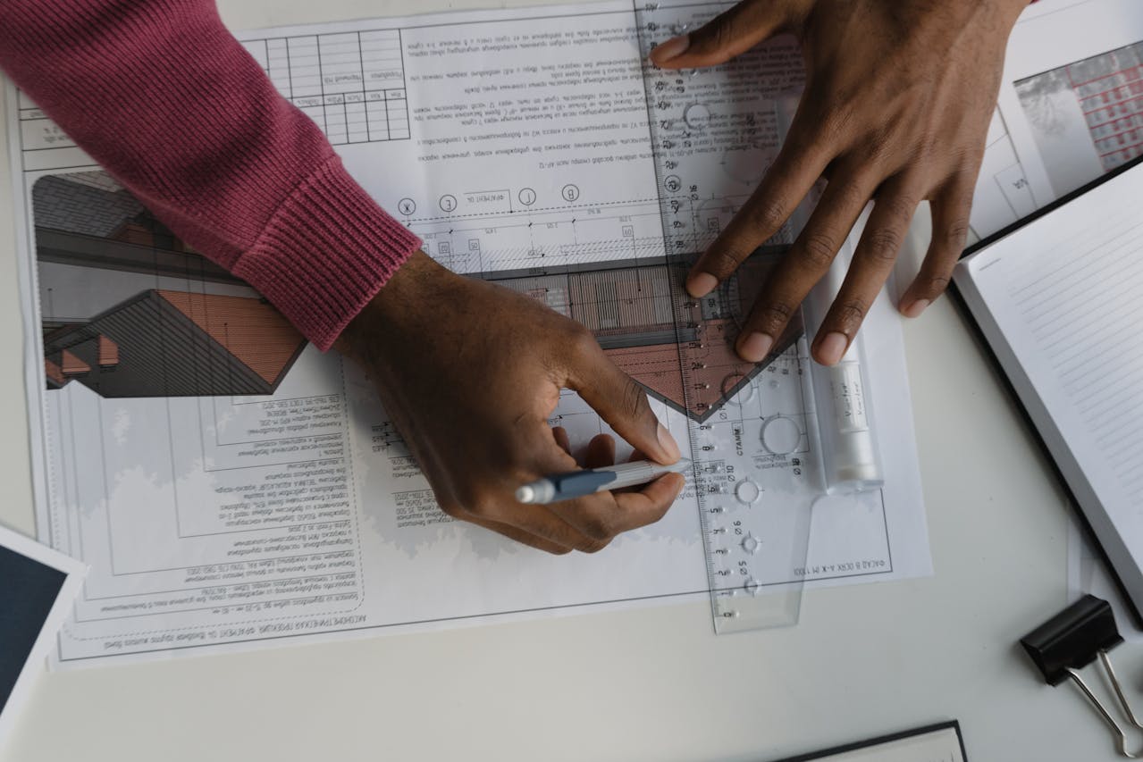 Mãos desenhando projetos arquitetônicos otimizados com régua e plantas técnicas sobre a mesa