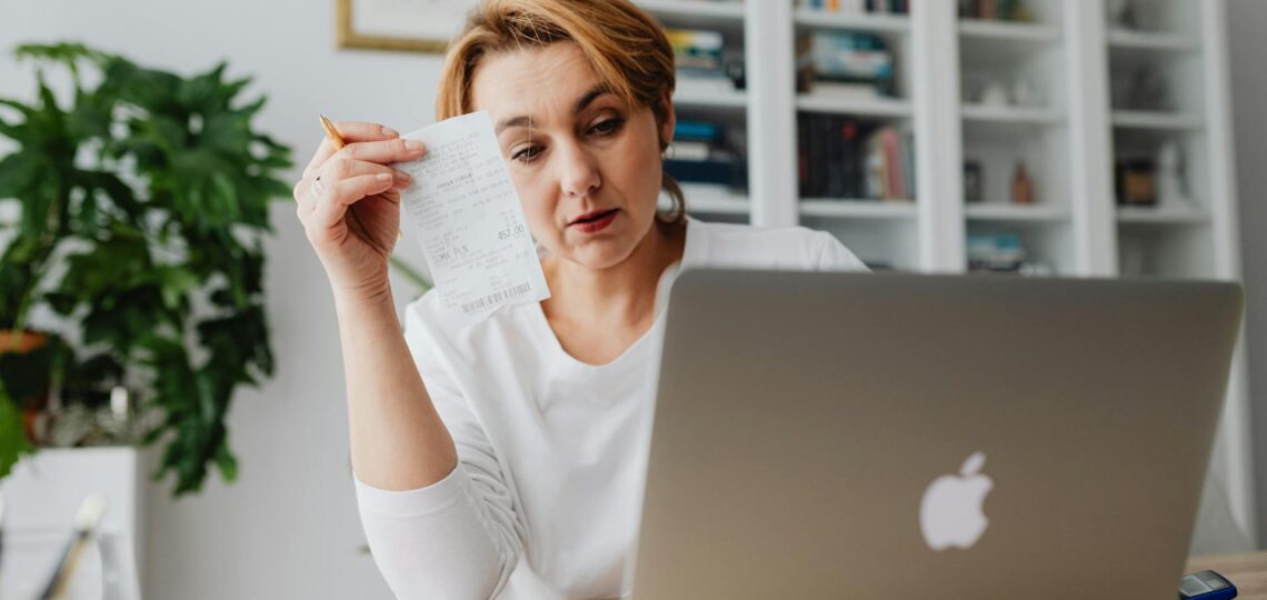 Mulher analisa recibo em frente ao notebook, representando desafios e soluções na automatização da contabilidade digital.