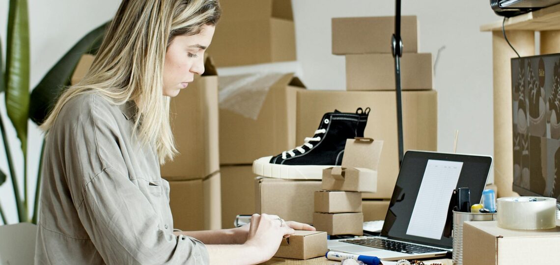 Empreendedora organizando pedidos de e-commerce com caixas e laptop