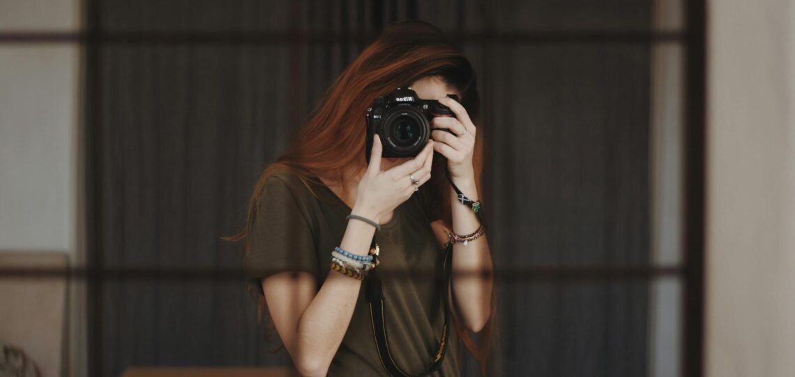 Mulher fotógrafa criativa com câmera Nikon em ambiente interno, simbolizando expressão artística e autenticidade visual.