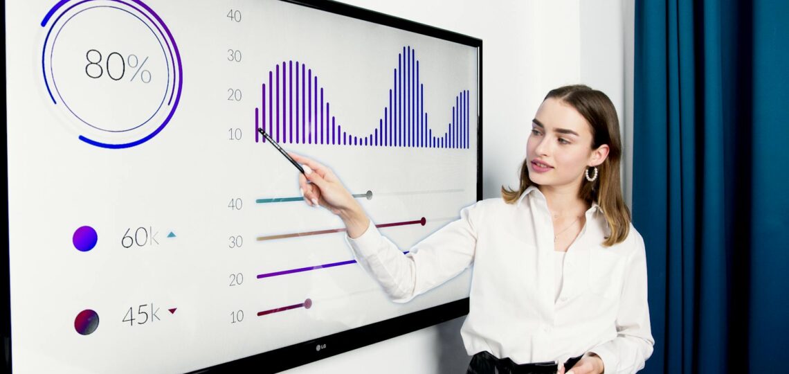 Mulher apresentando dados de performance em tela digital durante treinamento corporativo.