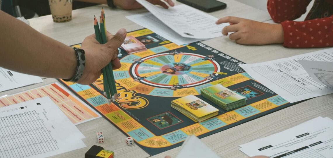 Pessoas jogando jogo de tabuleiro educativo sobre finanças pessoais com planilhas e dados sobre a mesa