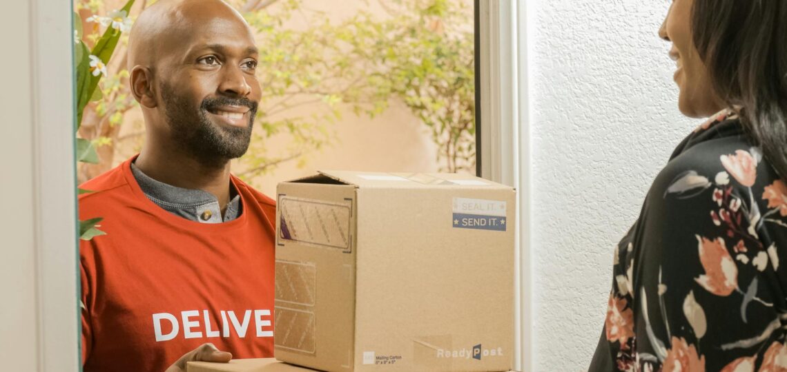 Entregador sorridente realizando entrega eficiente de encomendas em domicílio.