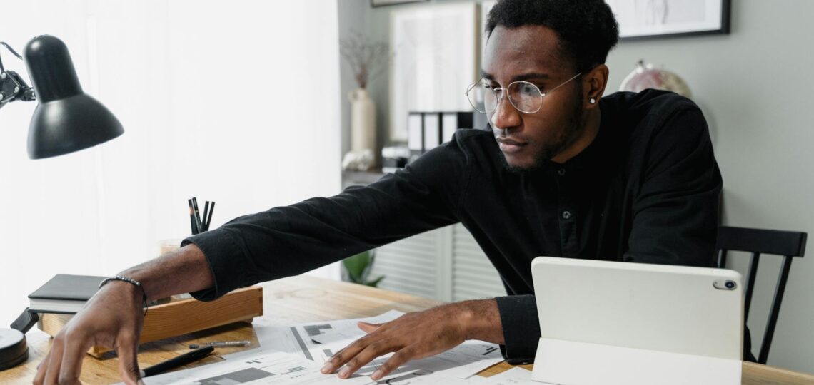 Profissional analisando documentos contábeis com uso de tecnologia digital em escritório moderno.