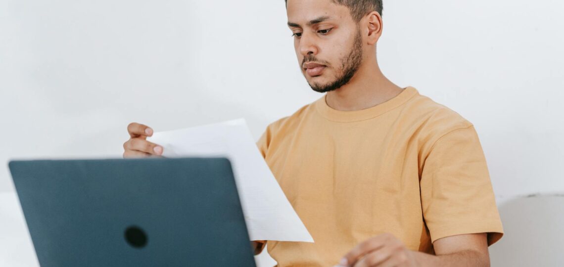 Jovem analisando finanças pessoais com notebook e documentos.