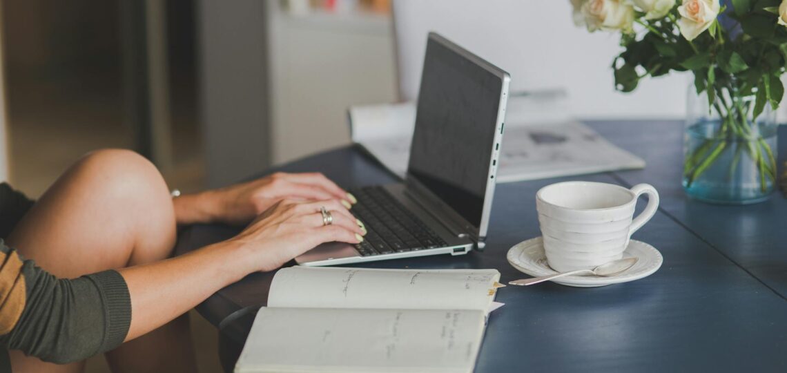 Mulher digitando em notebook com café e caderno sobre a mesa, simbolizando produtividade com IA no copywriting