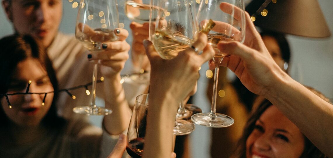 Grupo de amigos brindando em festa iluminada com taças de vinho e sorrisos