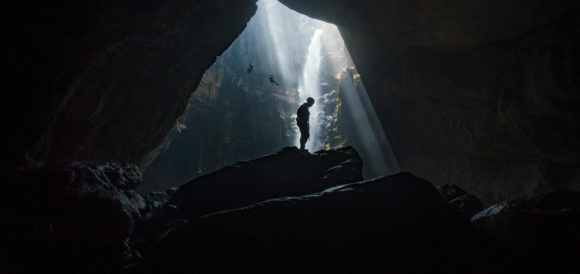 Explorador em caverna com luz natural e cachoeira, representando viagens personalizadas com inteligência artificial.