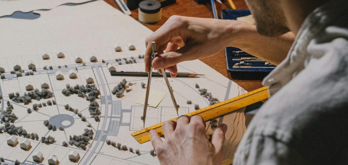 Arquiteto ajustando maquete urbana com compasso e régua sobre mesa de projeto detalhado.