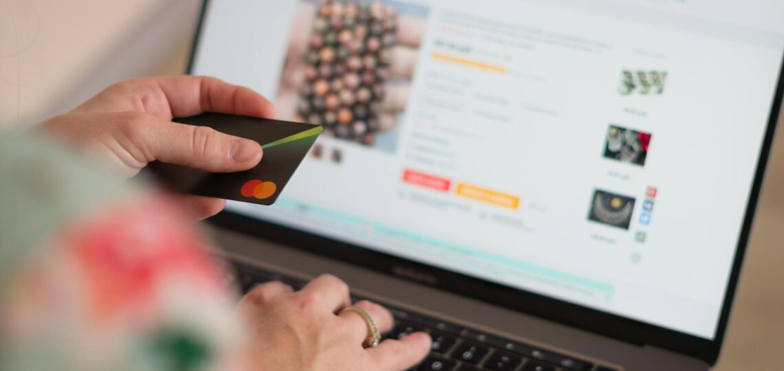 Pessoa segurando cartão de crédito e fazendo compra online em loja virtual, representando e-commerce automatizado.