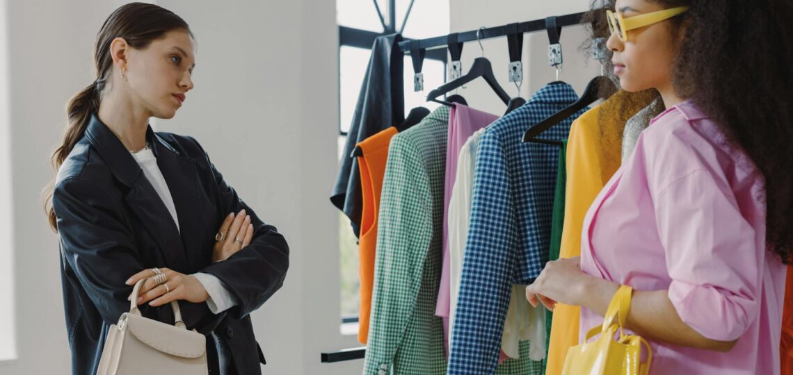 Duas mulheres analisando peças coloridas em um estúdio de moda, representando uma consultoria de estilo personalizada.