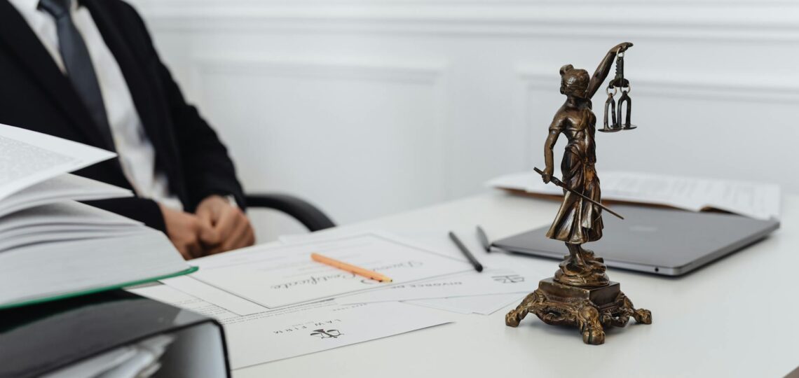 Advogado em escritório com balança da justiça sobre a mesa e documentos jurídicos ao fundo.