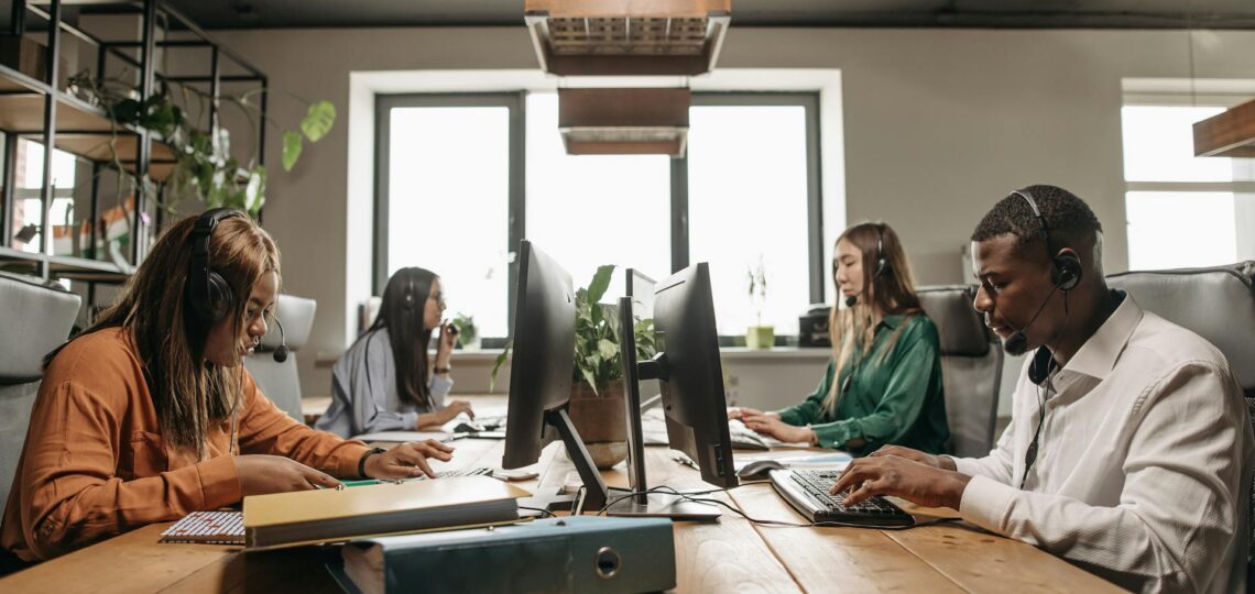 mesa com 4 pessoas com computadores trabalhando em um escritório