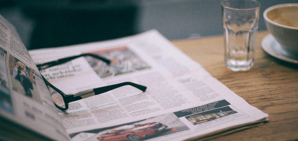 jornal sobre uma mesa desfocado e com um oculos sobre.