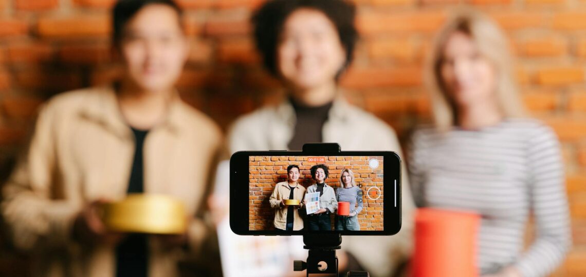 três mulheres desfocadas sendo filmadas por um celular em um tripé