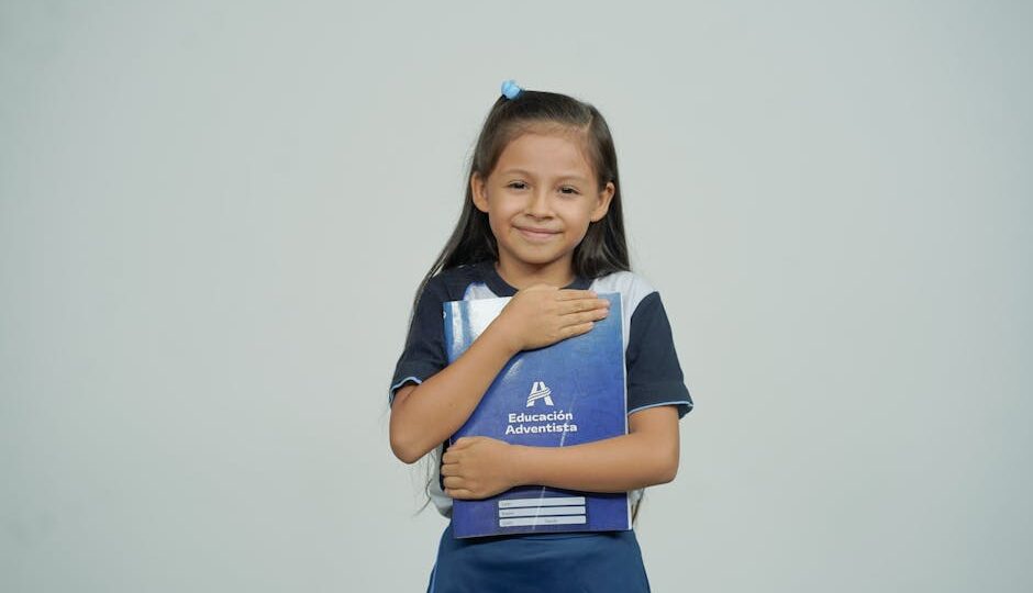 A young girl smiles while holding her school notebook, representing joy in education.