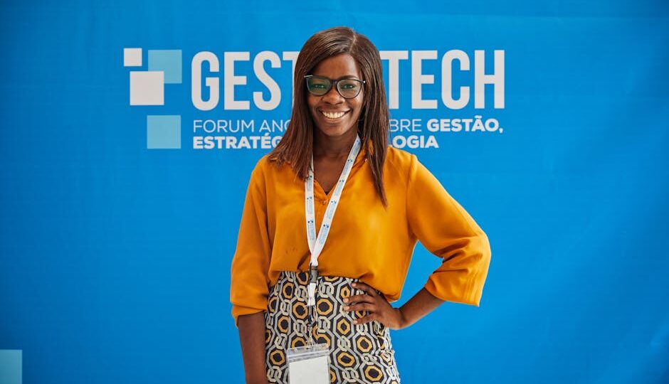 Smiling woman in orange blouse poses confidently at Gest Tech event backdrop.