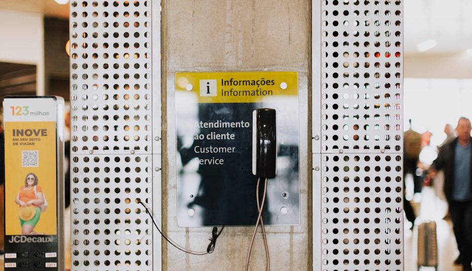 Public phone for customer service at a bustling station entrance with signage.
