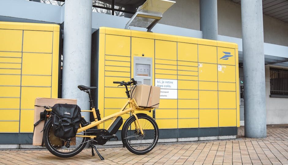 A yellow cargo e-bike loaded with parcels parked outside a package pickup station in France.