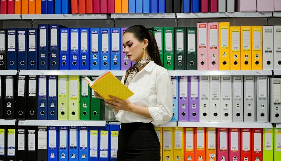 A young woman reads a file in front of a vibrant array of office binders.