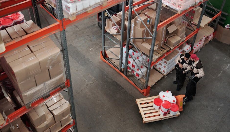 Workers managing inventory on shelves in a warehouse, viewed from above.