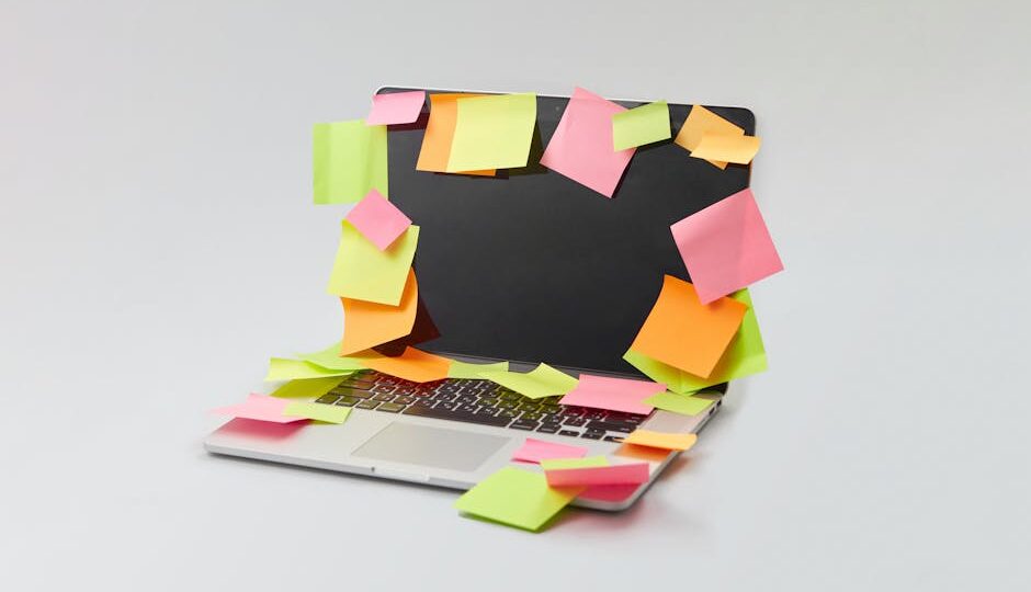 A laptop covered with colorful sticky notes for organization and reminders on a white surface.