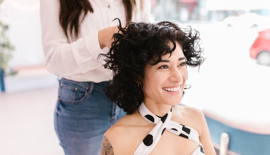 Joyful woman with curly hair being styled in a modern salon setting.