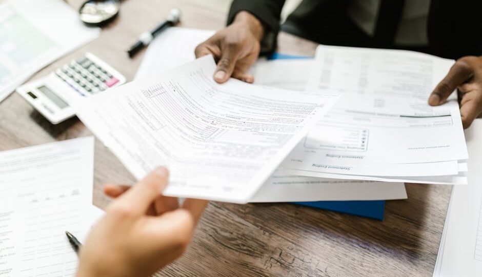 Two professionals exchanging documents in an office setting, focusing on paperwork and data analysis.