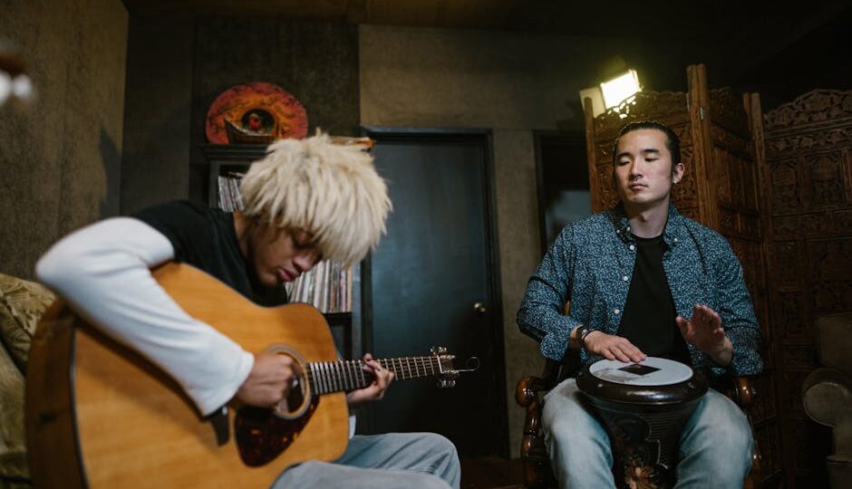 Two musicians playing guitar and drum in a cozy recording studio setting.