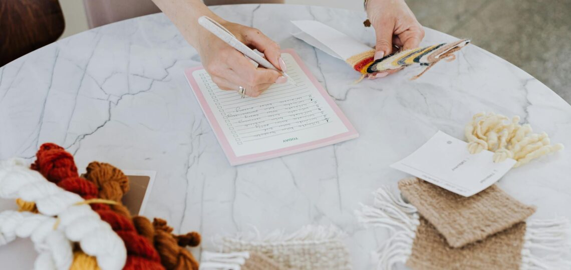 mao de mulher segurando caneta e fazendo anotações em um bloco sobre a mesa