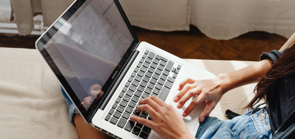 mulher sentada na poltrona escrevendo em um blog em um laptop sobre suas pernas