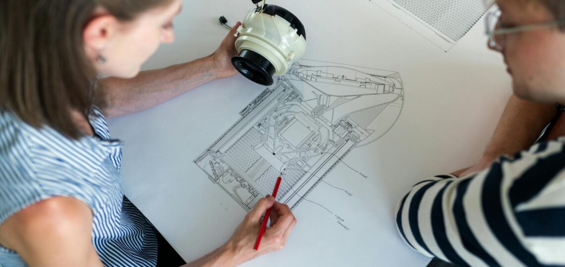 mulher conversa com homem sobre uma prancheta analisando desenho técnico de um produto