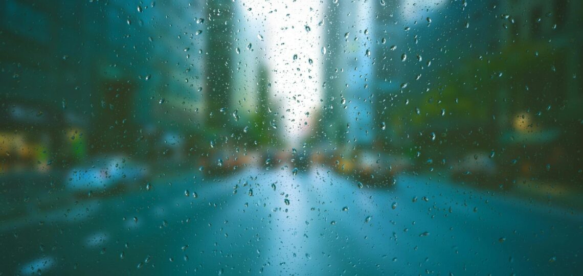Avenida em cidade grande sob ponto de vista do motorista dentro do carro, em dia de chuva, com imagem desfocada