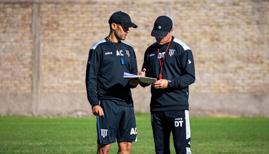 Two soccer coaches reviewing strategies on the field during the day.