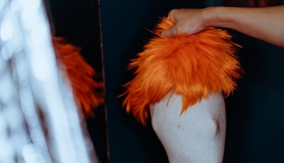 Close-up of an orange wig being placed on a mannequin head in a studio setting.