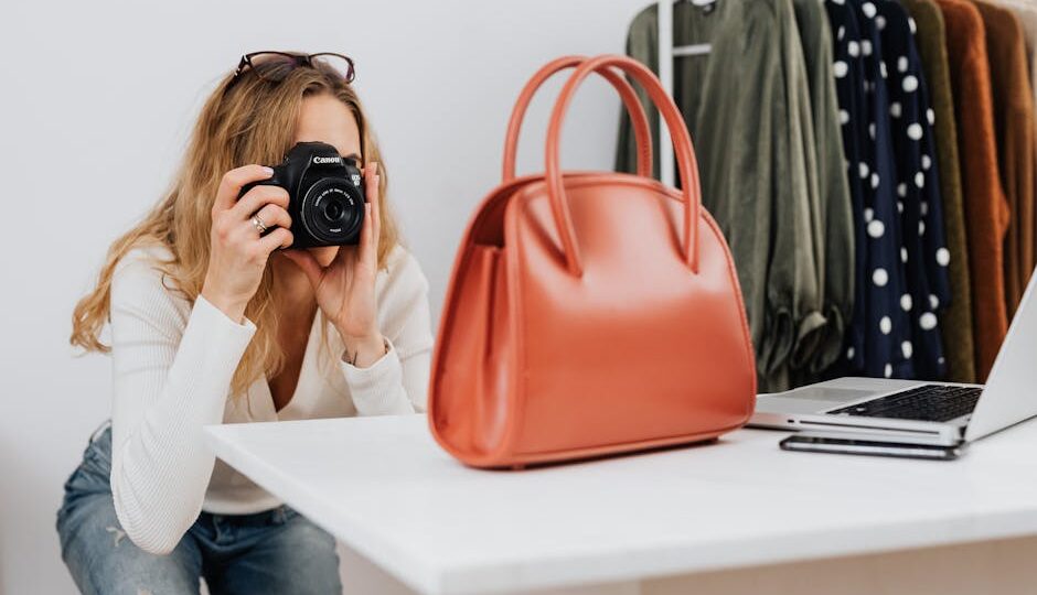 Caucasian woman capturing handbag photos for online fashion retail with camera.