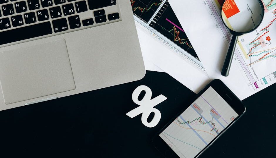 Overhead view of financial analysis tools with laptop, smartphone, and charts on a desk.