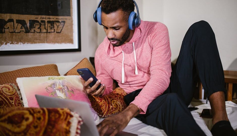 Adult man multitasking with laptop and phone, studying online in a comfortable setting.