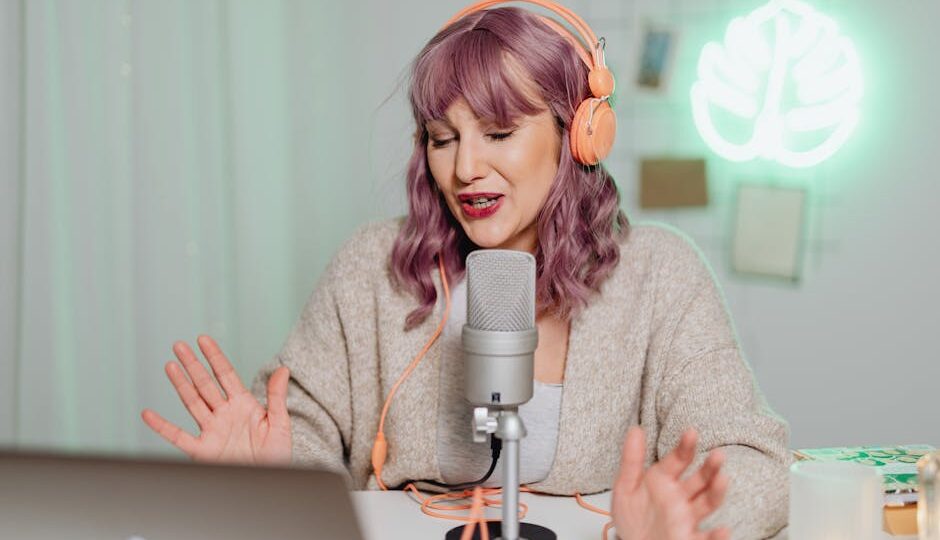 Woman podcasting indoors with headphones and microphone, engaging in recording or live stream.