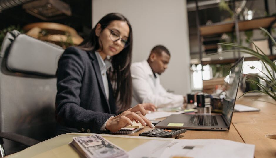 Two business professionals collaborating with a laptop and calculator in a modern office.