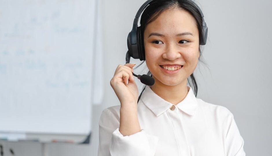 Asian woman smiling in a customer service role wearing a headset indoors.