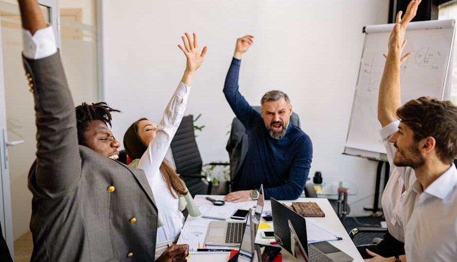 Diverse business team raising hands in excitement during a meeting in a modern office.