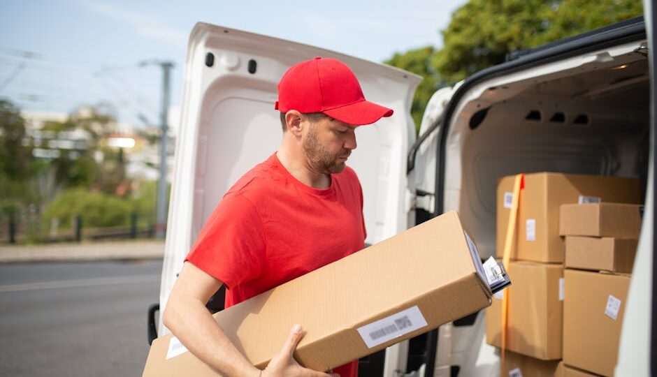 Courier in red uniform unloading packages from a delivery van on a sunny day.