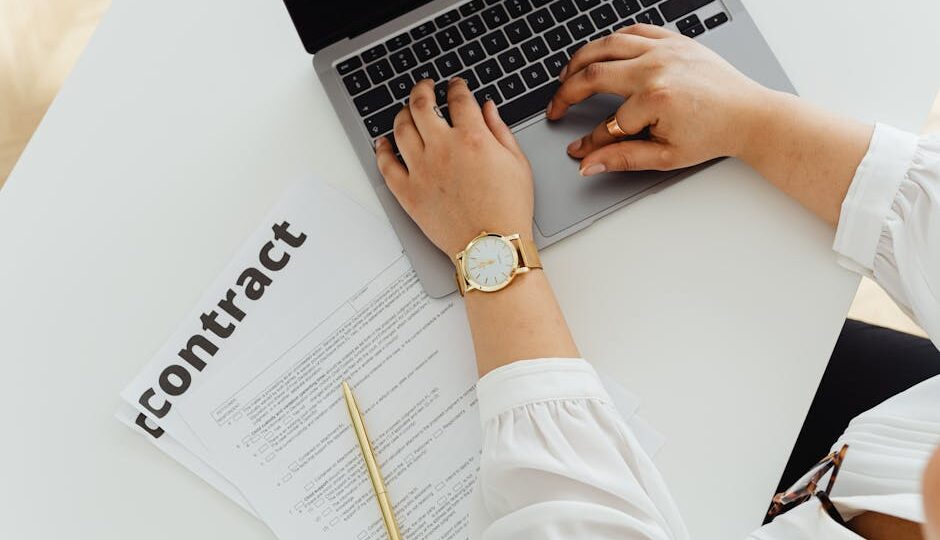 A woman using a laptop alongside a contract document on a desk, emphasizing business and legal themes.