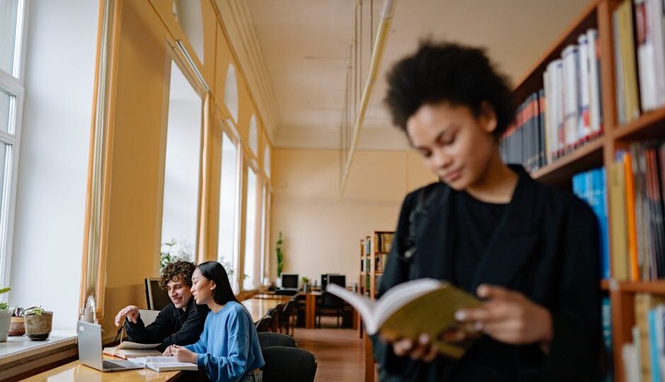 Students engaged in study sessions inside a university library, focusing on books and laptops.