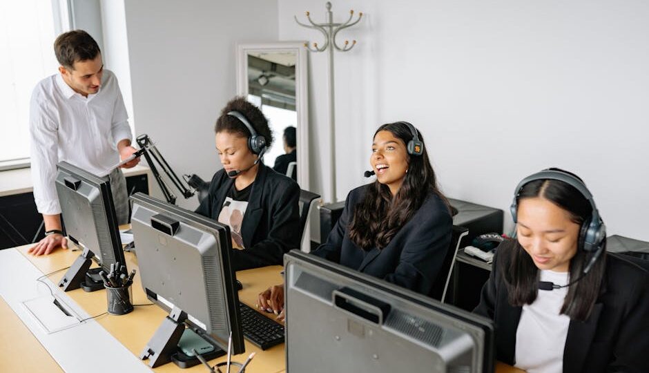 A diverse team of customer service representatives working in an office setting, wearing headsets and using computers.