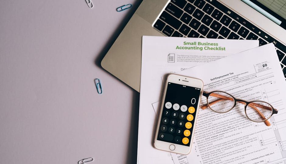 Flat lay of small business accounting tools including tax form, phone, and glasses on a desk.